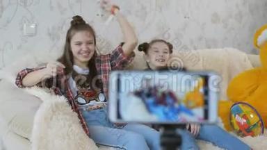 两个姐妹在智能手机拍摄视频前玩得很开心。 在家里`智能手机上拍摄一个孩子的视频博客。